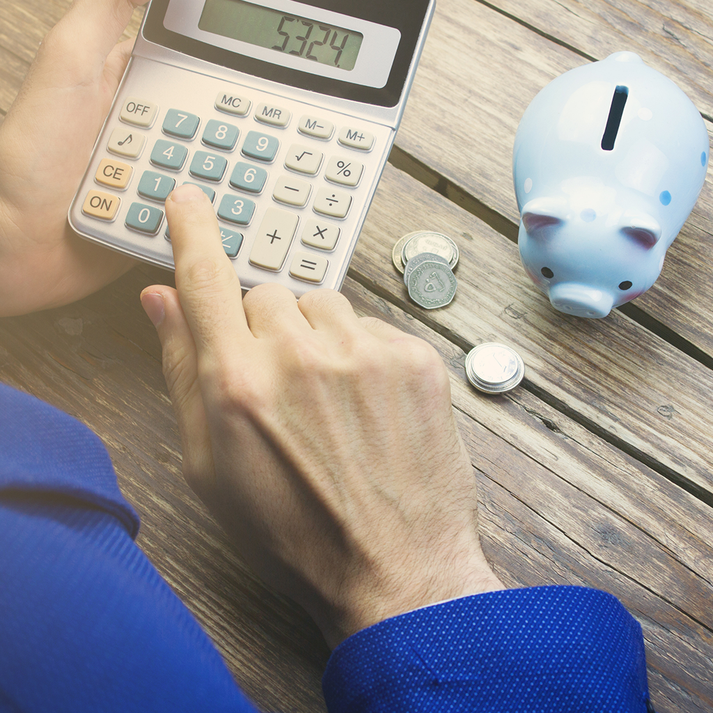 Person typing on a calculator next to a piggy bank.