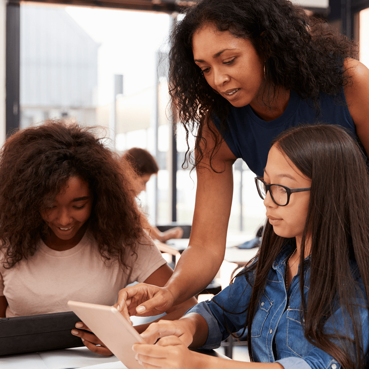 Woman teaching two young girls on tablets.