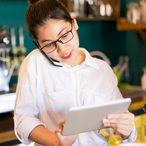 Barista banking on her phone and tablet.